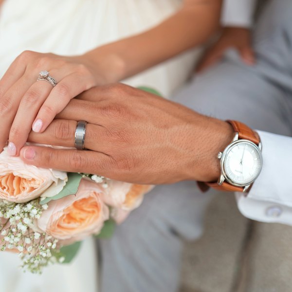 Mains des mariés avec leurs alliances, près d'un bouquet de roses