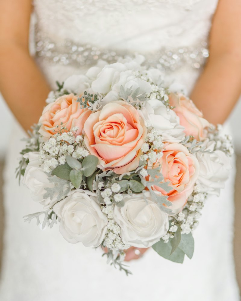 Mariée tenant un bouquet de roses pêche et blanches