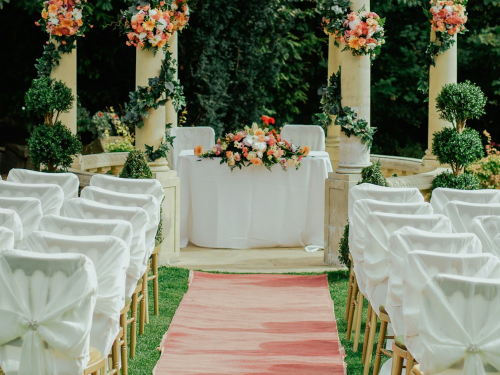 Cérémonie en plein air décorée de compositions florales, chaises habillées de blanc